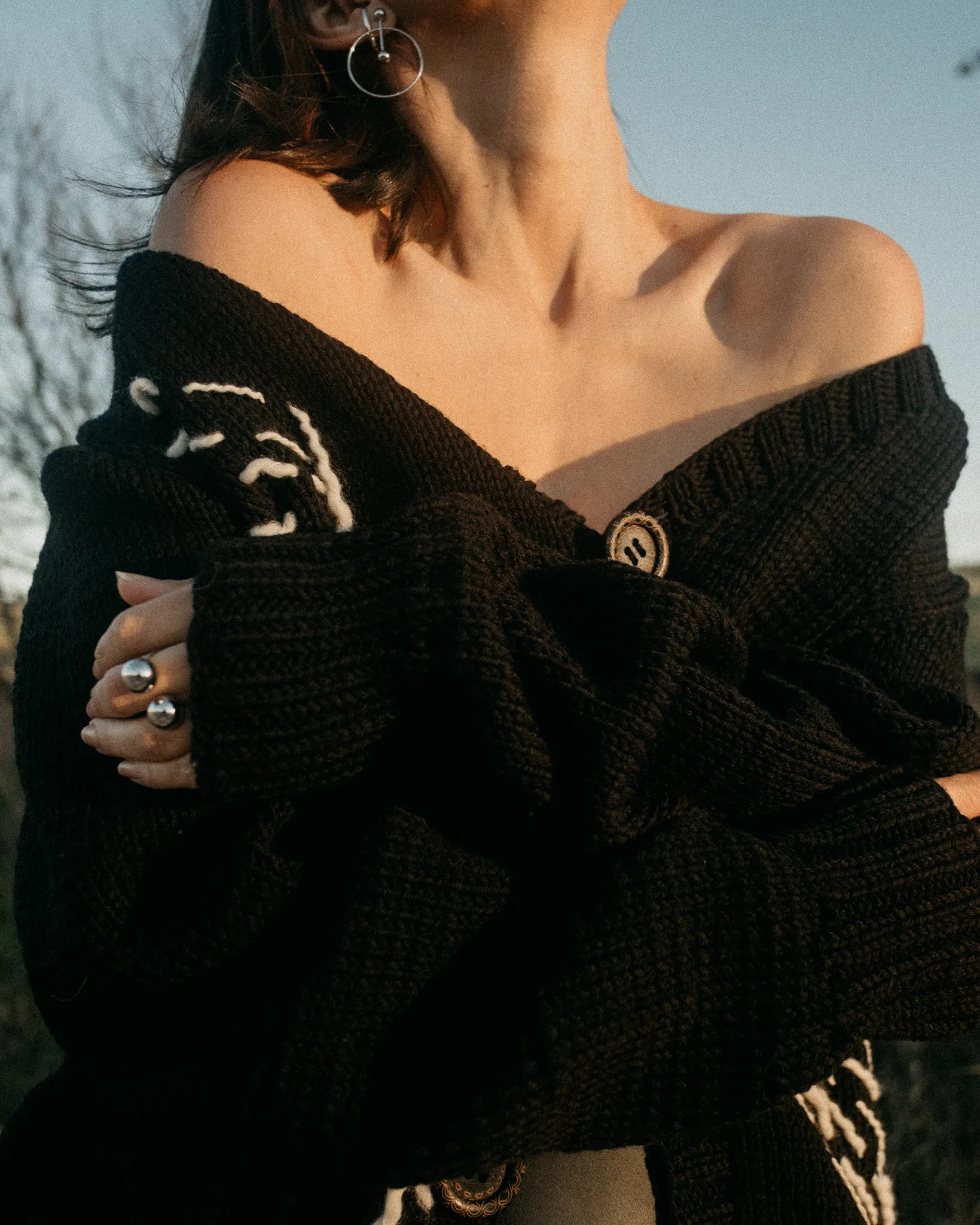 Model wearing Looking Friday black Italian merino wool Abstract Cardigan off the shoulder with white stitch accents and large buttons.