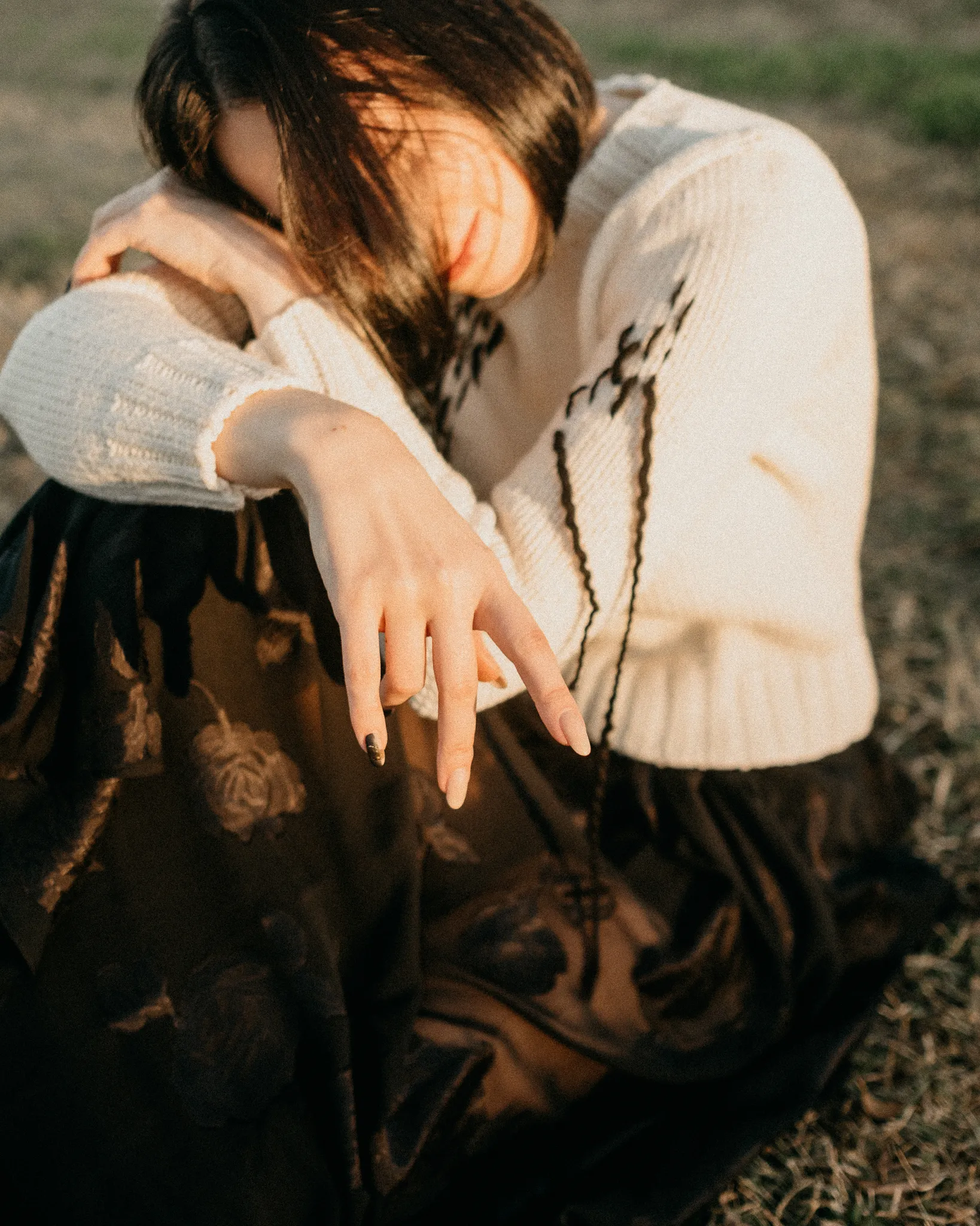 Model seated outdoors in Looking Friday cream Italian merino wool abstract sweater and black floral rose jacquard silk skirt.