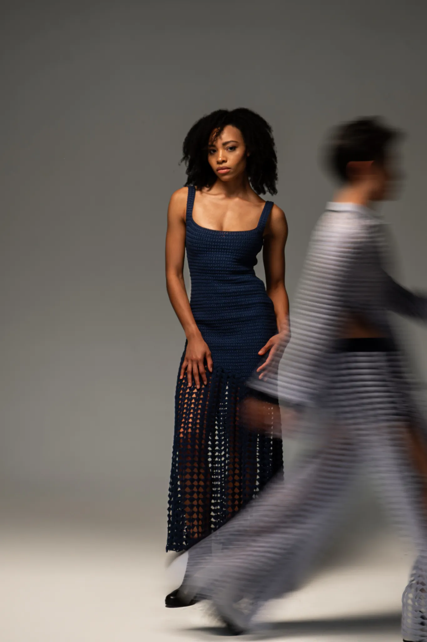 Model wearing the Looking Friday navy blue Crochet Fan Bodycon Dress with a fitted bodice and open-lattice fan hem, captured with motion blur.