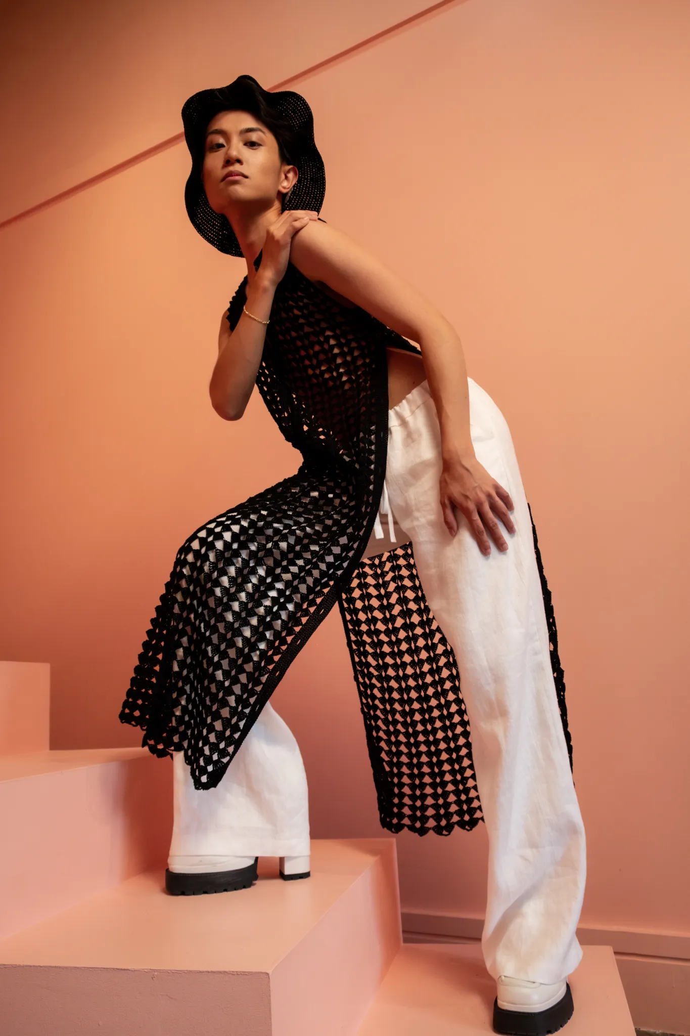 Model in Looking Friday black sleeveless Crochet Fan Tunic with deep side slits over white Linen Wide Leg Trousers.