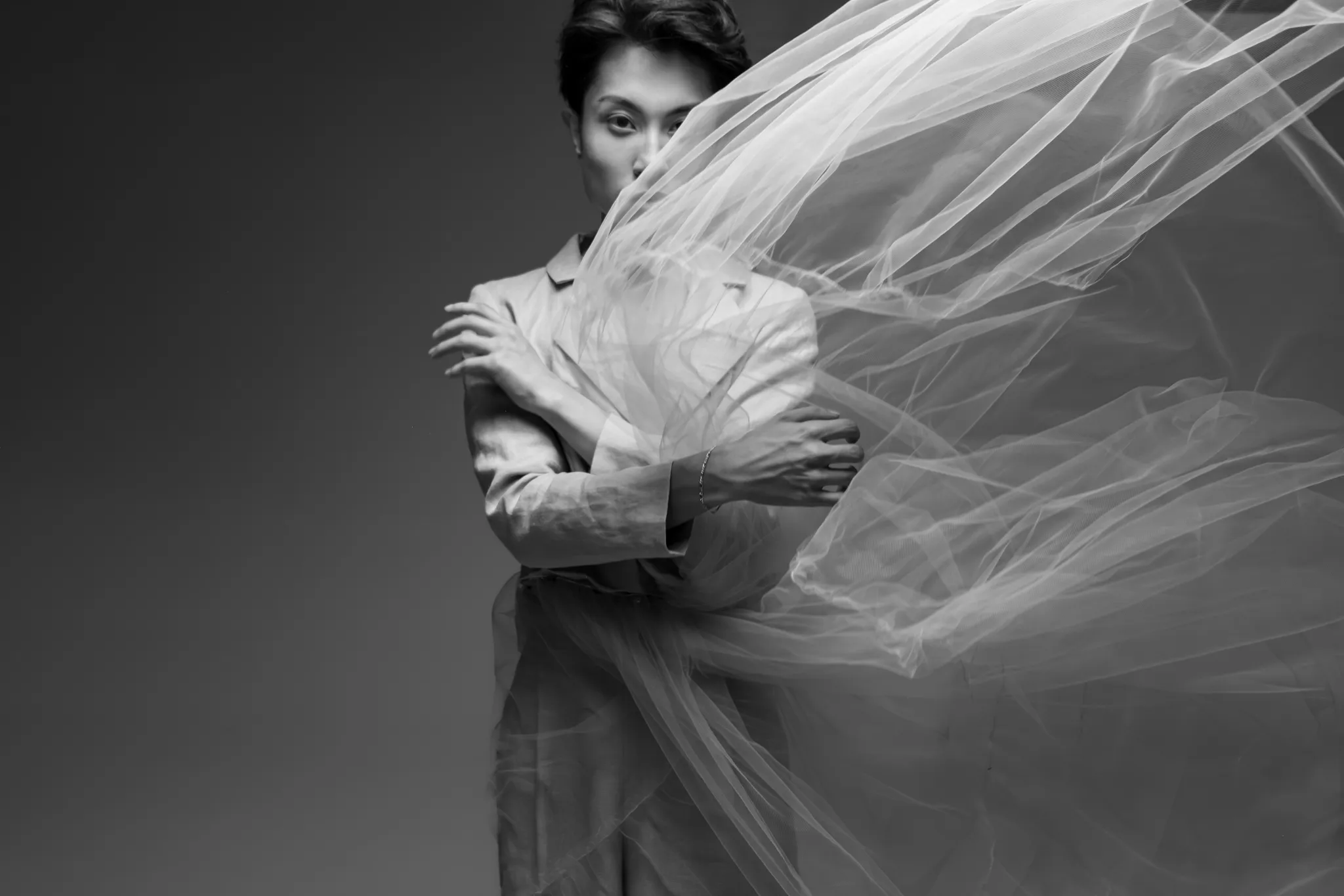 Model in a light grey tailored linen cropped jacket and wide-leg trousers wearing a flowing, dramatic sheer tulle skirt-train by Looking Friday.