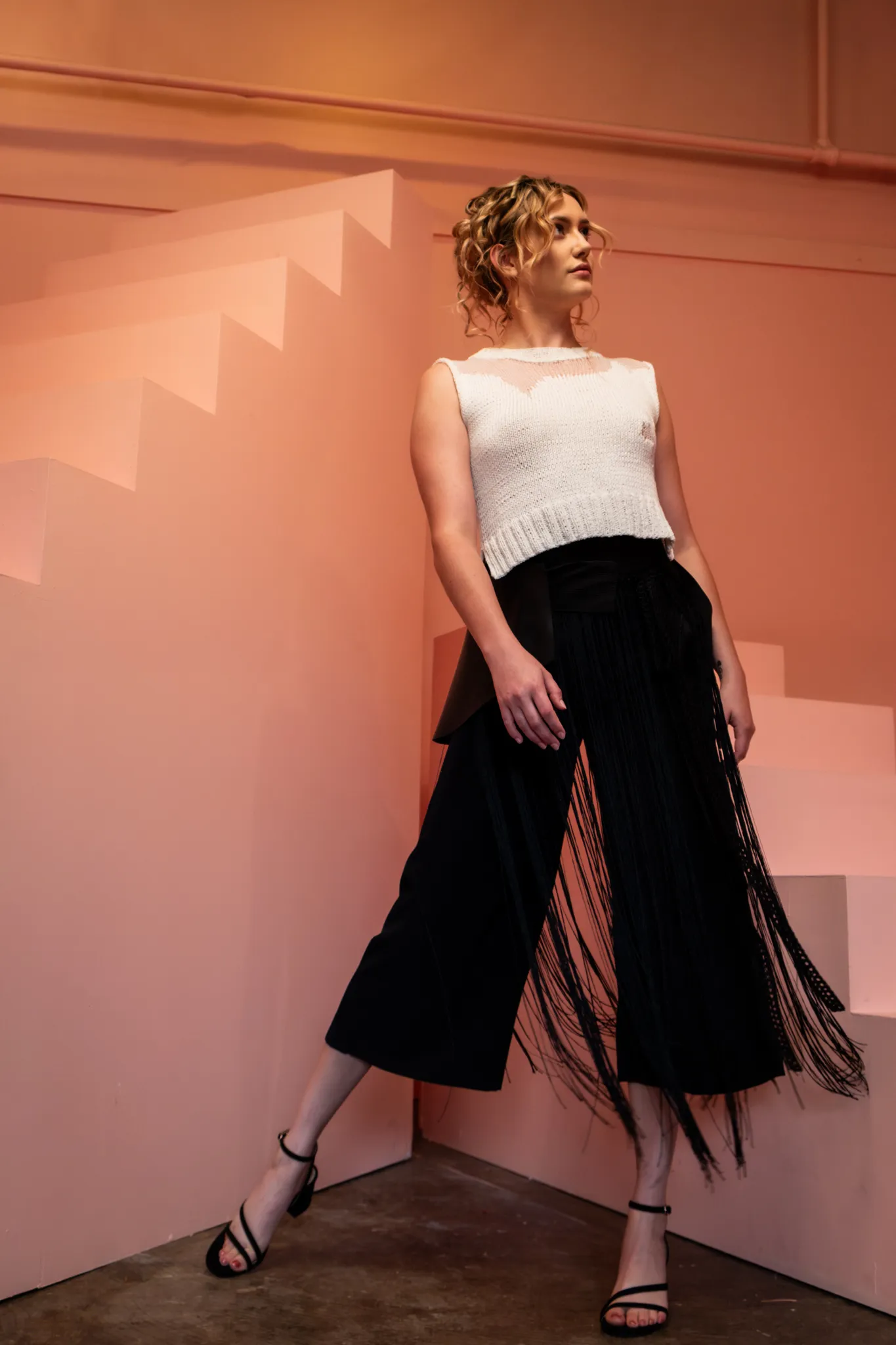 Model in Looking Friday black Silk Culottes layered with a Leather Belt, Fringe Crochet Belt, and white Distressed Knit Top.