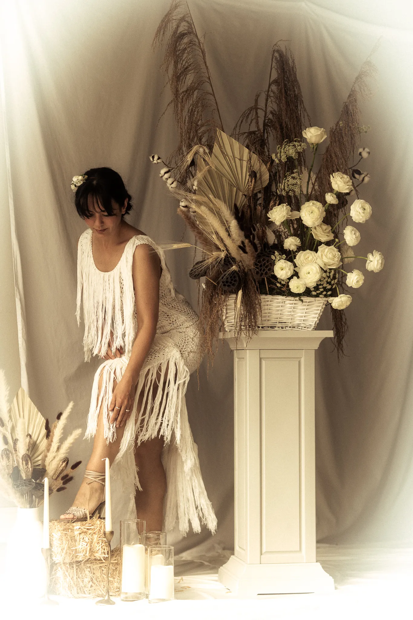 Full-length studio portrait of a bride wearing Looking Friday's Donna Gown, showcasing hand-knotted cotton fringe at the bust and a high-low asymmetrical fringe skirt in a romantic setting.