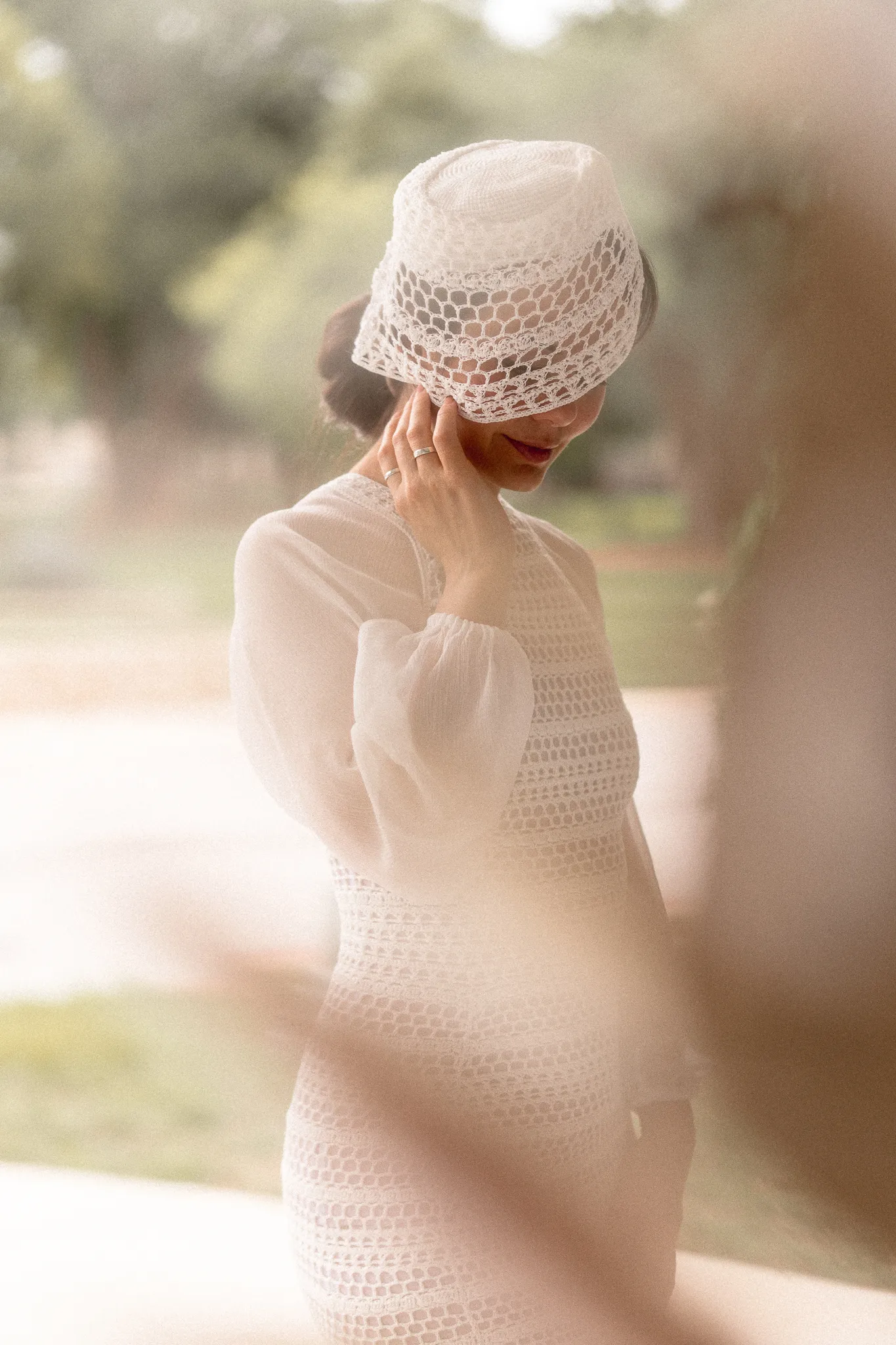 Close-up portrait of a bride in Looking Friday's Sophie Midi Dress, showcasing the organic cotton crochet bodice, sheer silk sleeves, and a custom crocheted pillbox hat veil.