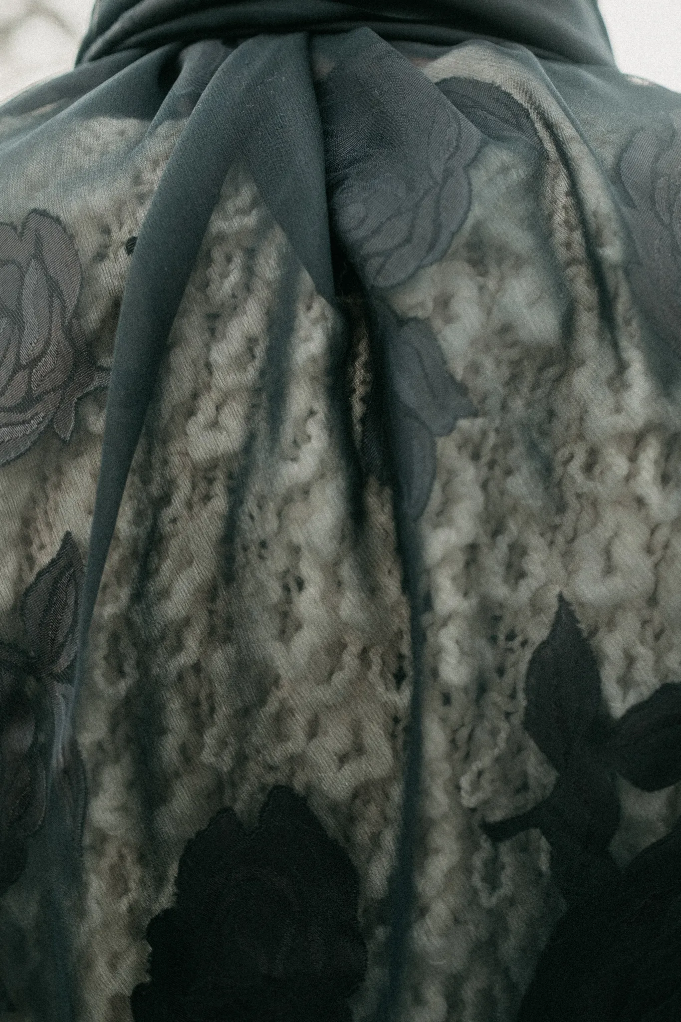 Macro texture detail of sheer black silk rose jacquard fabric layered over textured white knitwear.